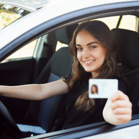 feliz estudiante conductor sentado moderno coche plateado mostrando permiso conducir
