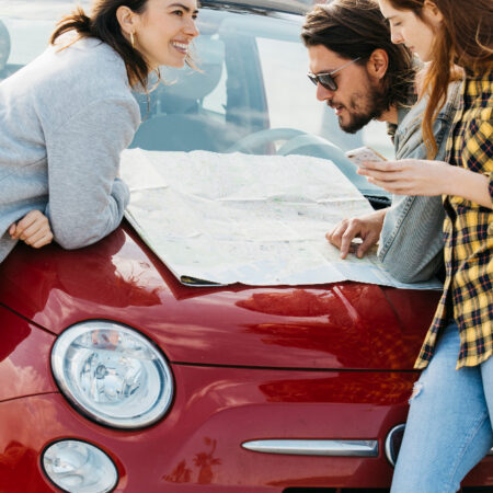 mujeres sonrientes telefono inteligente cerca hombre mirando mapa capo coche